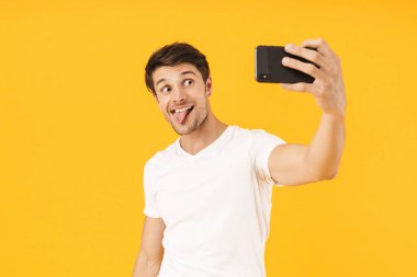 Rahat beyaz t-shirt Mutlu genç neşeli adam sarı arka plan üzerinde izole cep telefonu ile selfie çekmek.