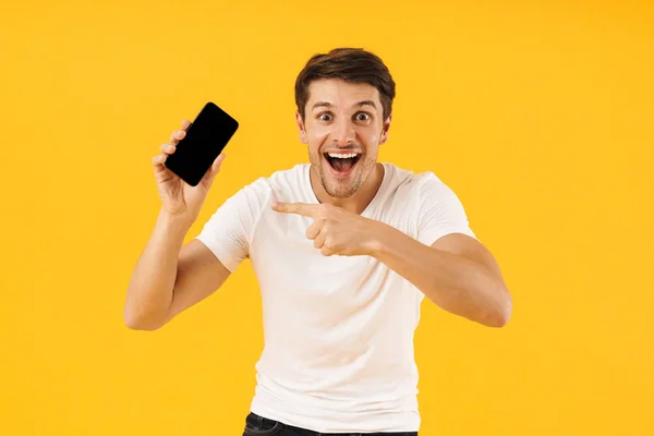 Chockad ung man i casual vit t-shirt med mobiltelefon isolerad över gul bakgrund. — Stockfoto
