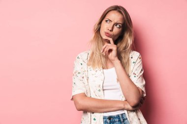 Düşünce hoşnutsuz genç sarışın sevimli kız pembe duvar arka plan üzerinde izole poz.