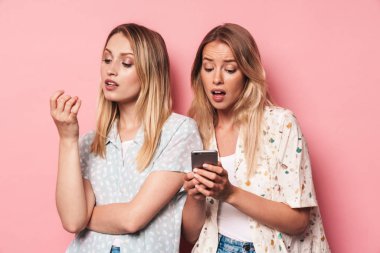 Onu kayıtsız kadın arkadaşı telefon pembe duvar arka plan üzerinde izole ekran gösteren cep telefonu kullanarak şok kız.
