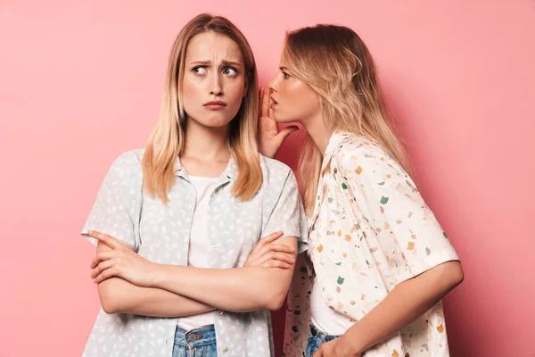 Descontentas rubias hermosas negativas mujeres amigas posando aisladas sobre fondo de pared rosa hablando entre sí chismorreando . —  Fotos de Stock