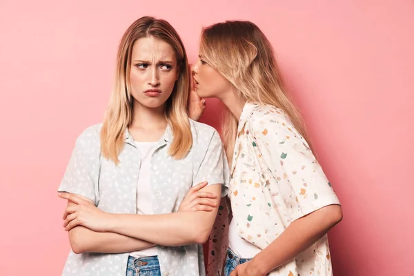 Негативні красиві блондинки жінки друзі позують ізольовані на фоні рожевих стін розмовляють між собою плітки . — стокове фото
