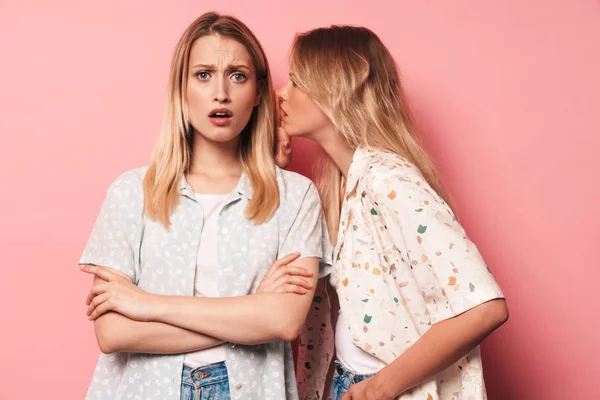 Descontentas rubias hermosas negativas mujeres amigas posando aisladas sobre fondo de pared rosa hablando entre sí chismorreando . —  Fotos de Stock