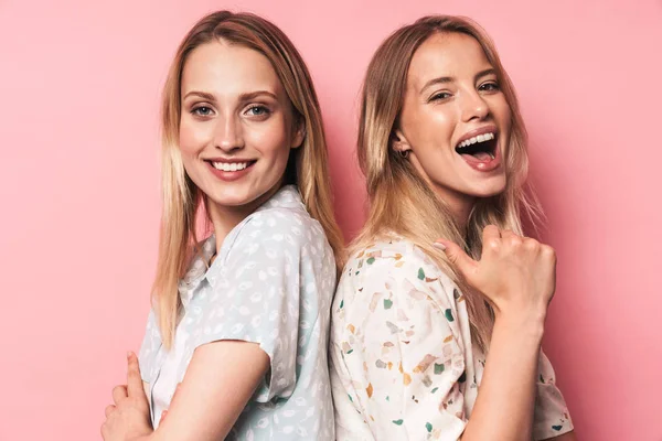 Vrolijke vrouw wijzend naar haar gelukkig mooie blonde vrouwen vriend zuster poseren geïsoleerd over roze muur achtergrond. — Stockfoto