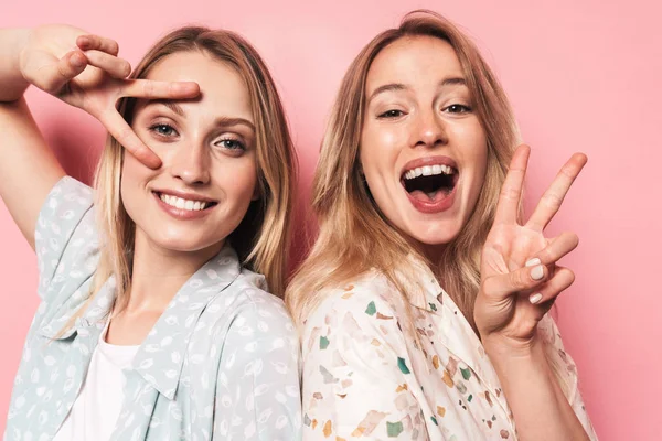 Vrolijke blij mooie blondjes vrouwen vrienden poseren geïsoleerd over roze muur achtergrond tonen vrede gebaar. — Stockfoto