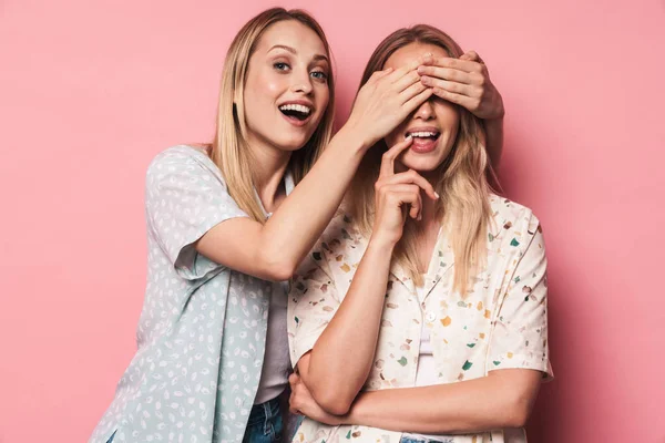 Χαρούμενο κορίτσι που καλύπτει τα μάτια της φίλης φίλη της αδερφής απομονωμένη πάνω από ροζ τοίχο φόντο. — Φωτογραφία Αρχείου