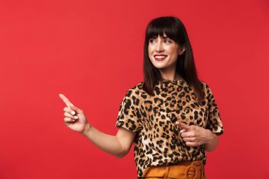 Kırmızı arka plan üzerinde izole poz gösteren hayvan baskılı gömlek giymiş genç kadın.