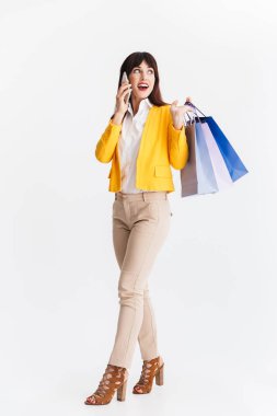 Genç iş kadını alışveriş çantaları tutan cep telefonu ile konuşurken beyaz arka plan üzerinde izole poz.