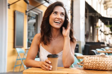 Rahat kafe açık havada otururken kağıt fincan kahve içme ve cep telefonu konuşurken mutlu güzel kadın Portresi