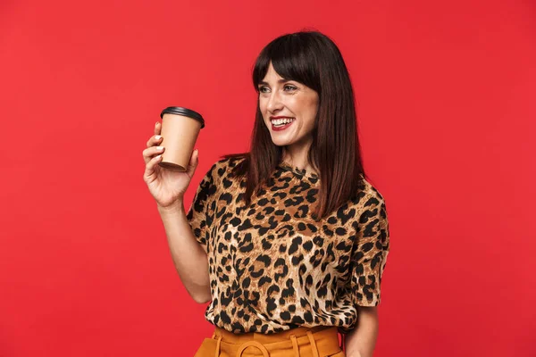 Bela feliz jovem mulher vestida com animal impresso camisa posando isolado sobre vermelho fundo beber café . — Fotografia de Stock