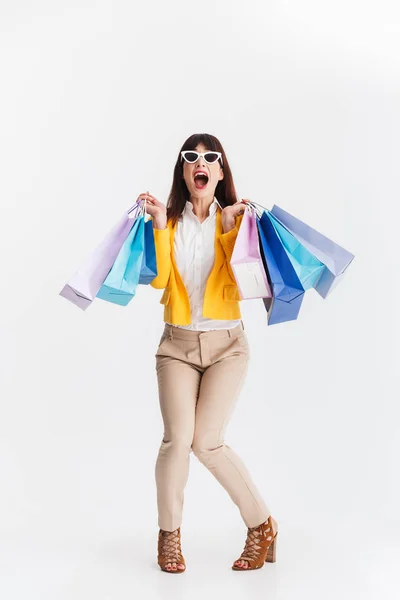 Impresionada joven mujer de negocios posando aislada sobre fondo blanco sosteniendo bolsas de compras . — Foto de Stock