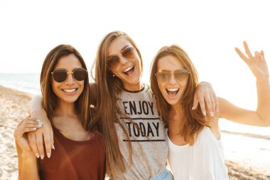 Üç neşeli kız plaj boyunca yürürken, eğleniyor