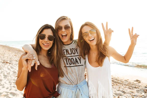 Drie vrolijke meiden die langs het strand wandelen, plezier hebben — Stockfoto