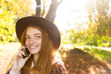 Mutlu mutlu tatlı genç öğrenci redhead kız sonbahar parkta cep telefonu kullanarak.