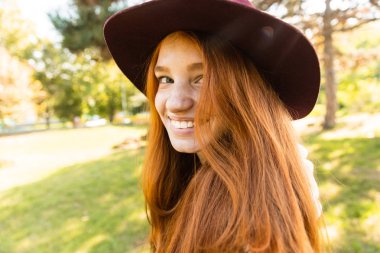 Neşeli gülümseyen mutlu genç öğrenci kızıl saçlı kız sonbahar parkta yürüyüş.