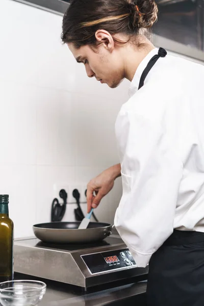 Hübsche junge Köchin kocht in der Küche drinnen. — Stockfoto