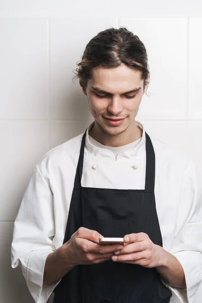 Jovem cozinheiro chef na cozinha usando telefone celular conversando . — Fotografia de Stock