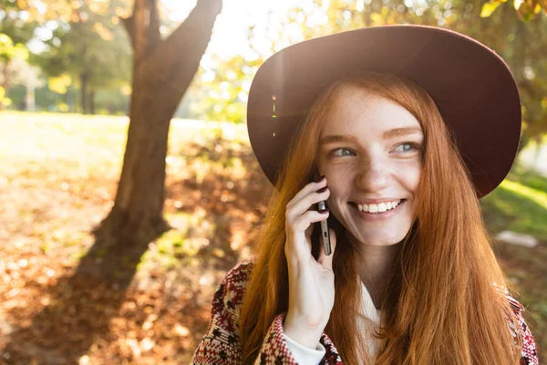 Boldog elégedett cutie fiatal diák vöröshajú lány őszi parkban mobiltelefon használata. — Stock Fotó