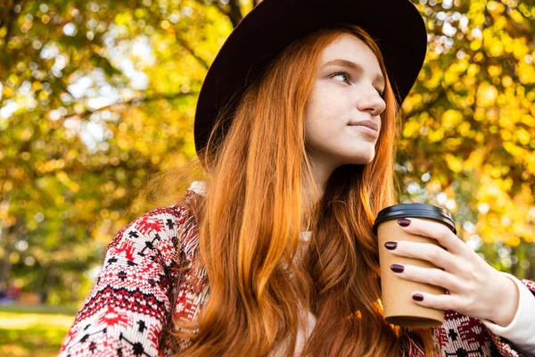 Optimista joven estudiante pelirroja en el parque de otoño beber café . —  Fotos de Stock