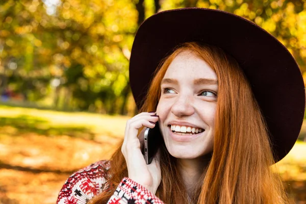 Feliz satisfeito cutie jovem estudante ruiva menina no outono parque usando telefone móvel . — Fotografia de Stock