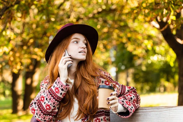 集中年轻学生红发女孩在秋天公园说话用手机喝咖啡. — 图库照片
