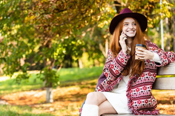 Pozitif memnun mutlu neşeli genç öğrenci redhead kız sonbahar parkta cep telefonu kahve içme ile konuşurken. — Stok fotoğraf