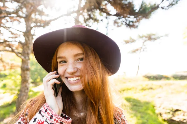 Boldog elégedett cutie fiatal diák vöröshajú lány őszi parkban mobiltelefon használata. — Stock Fotó