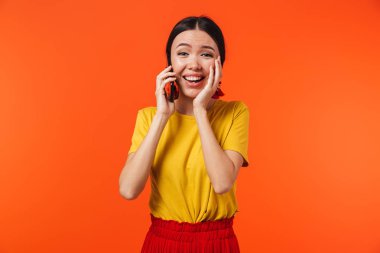 Güzel mutlu genç kadın cep telefonu ile konuşurken turuncu duvar arka plan üzerinde izole poz.