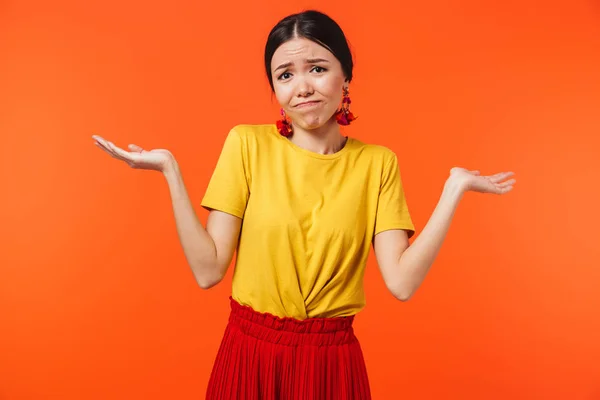 Verward displease jonge vrouw poseren geïsoleerd over oranje muur achtergrond. — Stockfoto