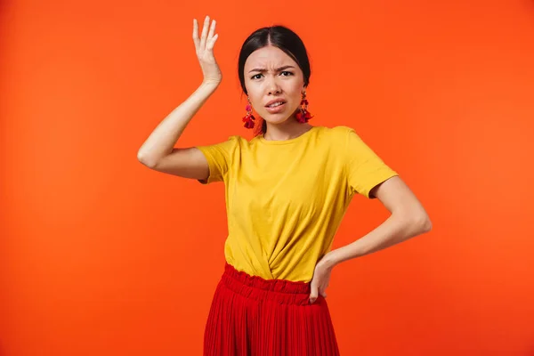 Verward displease jonge vrouw poseren geïsoleerd over oranje muur achtergrond. — Stockfoto