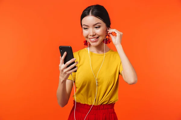 Bella giovane donna posa isolata su sfondo arancione parete utilizzando il telefono cellulare musica di ascolto . — Foto Stock