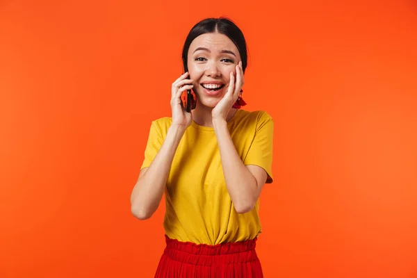 아름 다운 행복 한 젊은 여자 포즈 고립 된 오렌지 벽 배경 이야기 로 휴대 전화. — 스톡 사진