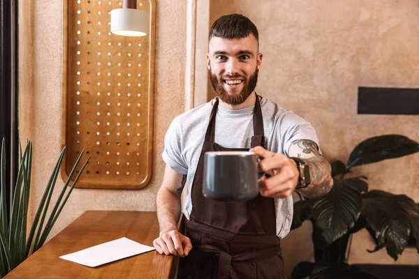 Hombres alegres barista usando delantal de pie en la cafetería —  Fotos de Stock