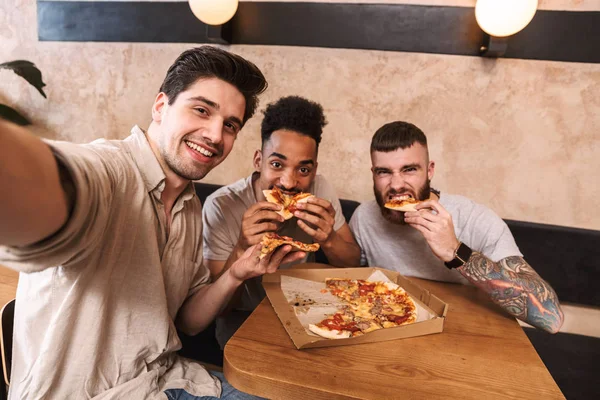 Tres hombres alegres comiendo pizza en la mesa del café — Foto de Stock