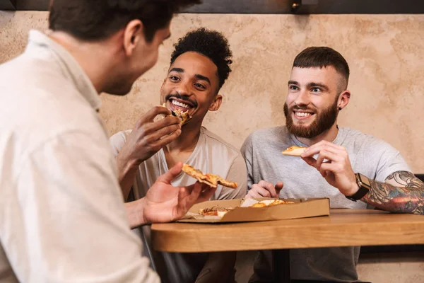 Tres hombres alegres comiendo pizza en la mesa del café — Foto de Stock