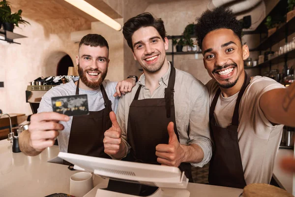 Três baristas homens alegres em pé atrás do balcão — Fotografia de Stock