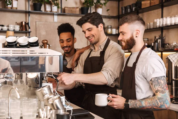 Drie vrolijke mannelijke barista's die in de koffiebar staan — Stockfoto