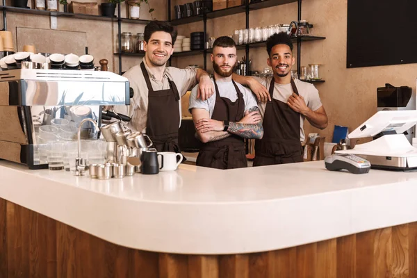 Três animados baristas masculinos em pé no café — Fotografia de Stock