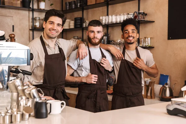 Drie vrolijke mannelijke barista's die in de koffiebar staan — Stockfoto