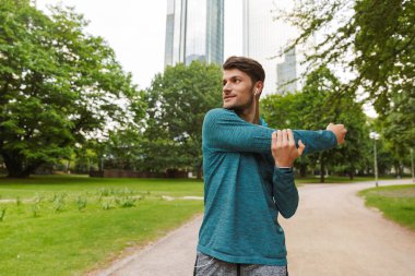 Spor yakışıklı adam kulaklık ile müzik dinleme ve şehir parkı kolunu germe Fotoğrafı