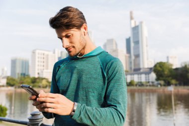 Şehir gezinti yakınında çalışırken cep telefonu ve kulaklık kullanarak odaklanmış adam Fotoğrafı