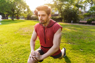 Şehir parkında çalışırken kulaklık kullanan ve egzersiz yapan konsantre adamın fotoğrafı
