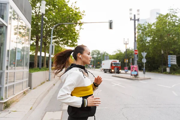 Foto de mujer deportiva agradable escuchando música con auriculares y corriendo en la calle de la ciudad — Foto de Stock