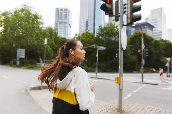Foto der sportlichen fokussierten Frau, die mit Kopfhörern Musik hört und auf der Straße läuft — Stockfoto