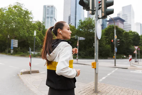 Φωτογραφία της σπορ εστιασμένη γυναίκα ακούγοντας μουσική με ακουστικά και τρέξιμο στο δρόμο της πόλης — Φωτογραφία Αρχείου