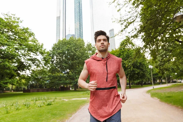Şehir parkında koşarken kulaklıkla müzik dinleyen yakışıklı adamın fotoğrafı