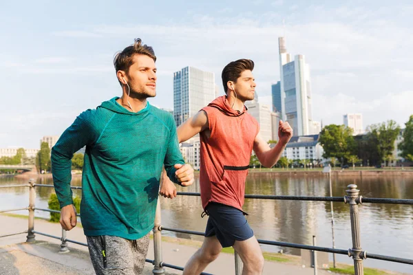 İki güçlü yakışıklı erkek egzersiz yapıyor ve şehir nehir üzerinde çalışan Fotoğraf