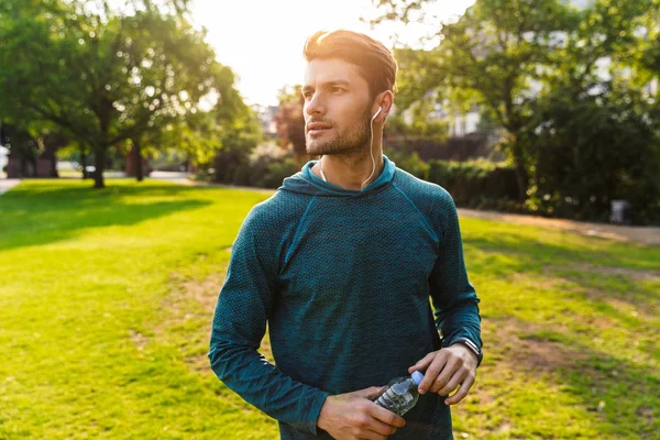 심각한 젊은 강한 스포츠맨 야외 에서 공원 청취 음악 과 이어폰 마시는 물. — 스톡 사진