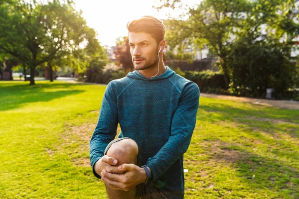 Ciddi sporcu parkta kulaklıkile müzik dinlerken bacaklar için egzersizyapmak açık havada.