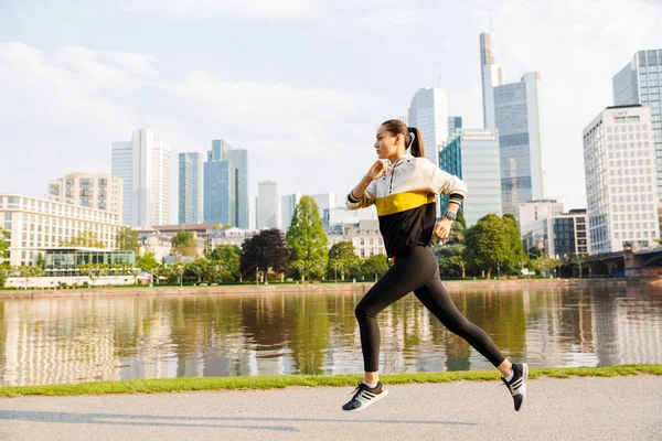 Foto de la hermosa mujer deportiva corriendo mientras hace ejercicio cerca de la orilla del río de la ciudad — Foto de Stock